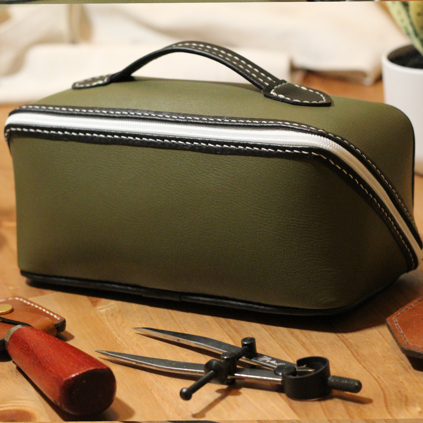 Handmade leather dopp kit made using a DIY pattern surrounded by leathercraft tools on a wooden table