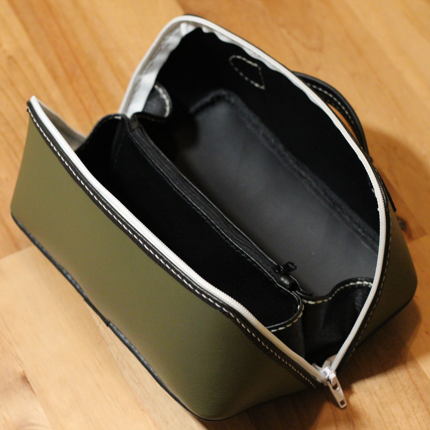 Handmade opened leather dopp kit made using a DIY pattern surrounded by leathercraft tools on a wooden table
