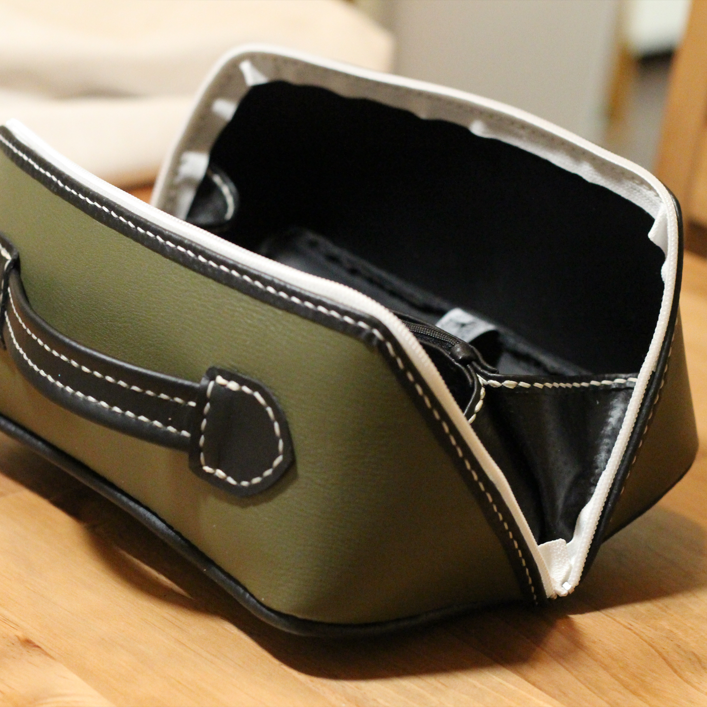 Handmade opened leather dopp kit made using a DIY pattern surrounded by leathercraft tools on a wooden table