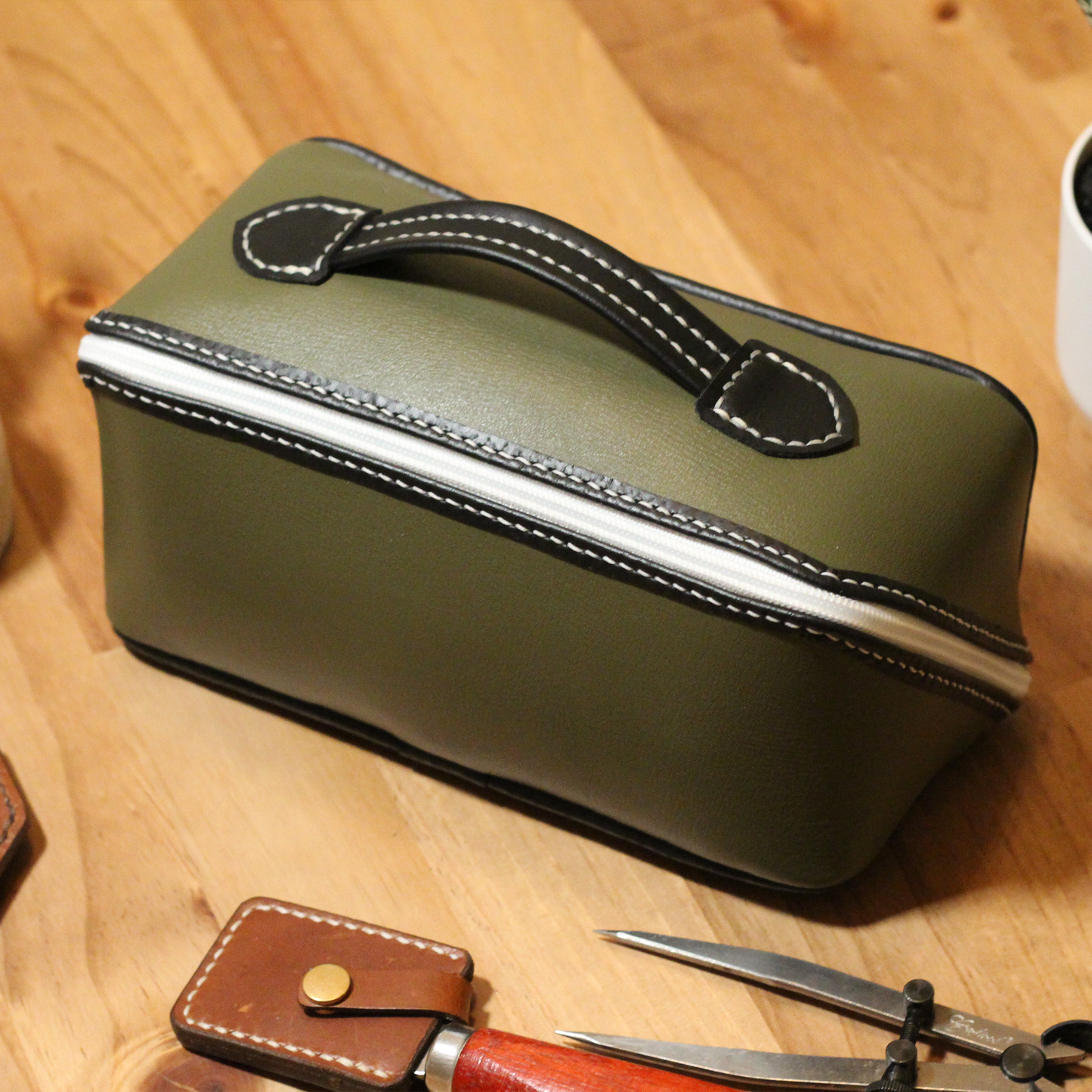 Handmade leather dopp kit made using a DIY pattern surrounded by leathercraft tools on a wooden table