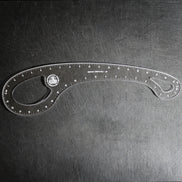 A clear plastic angle ruler with measurement markings and a circular logo, photographed on a dark textured surface.