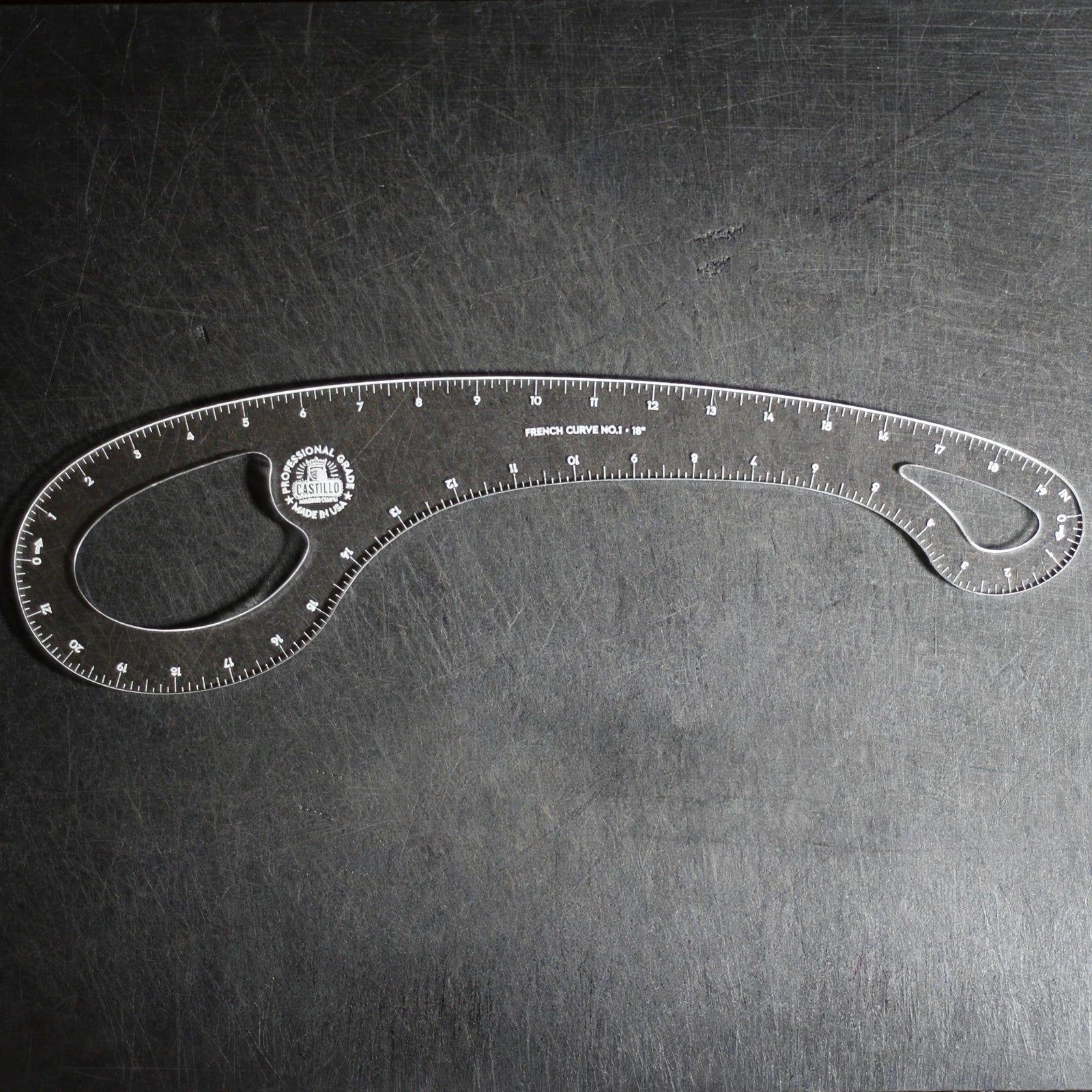 A clear plastic angle ruler with measurement markings and a circular logo, photographed on a dark textured surface.
