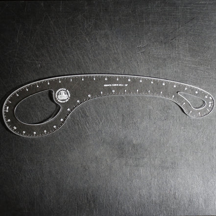 A clear plastic angle ruler with measurement markings and a circular logo, photographed on a dark textured surface.