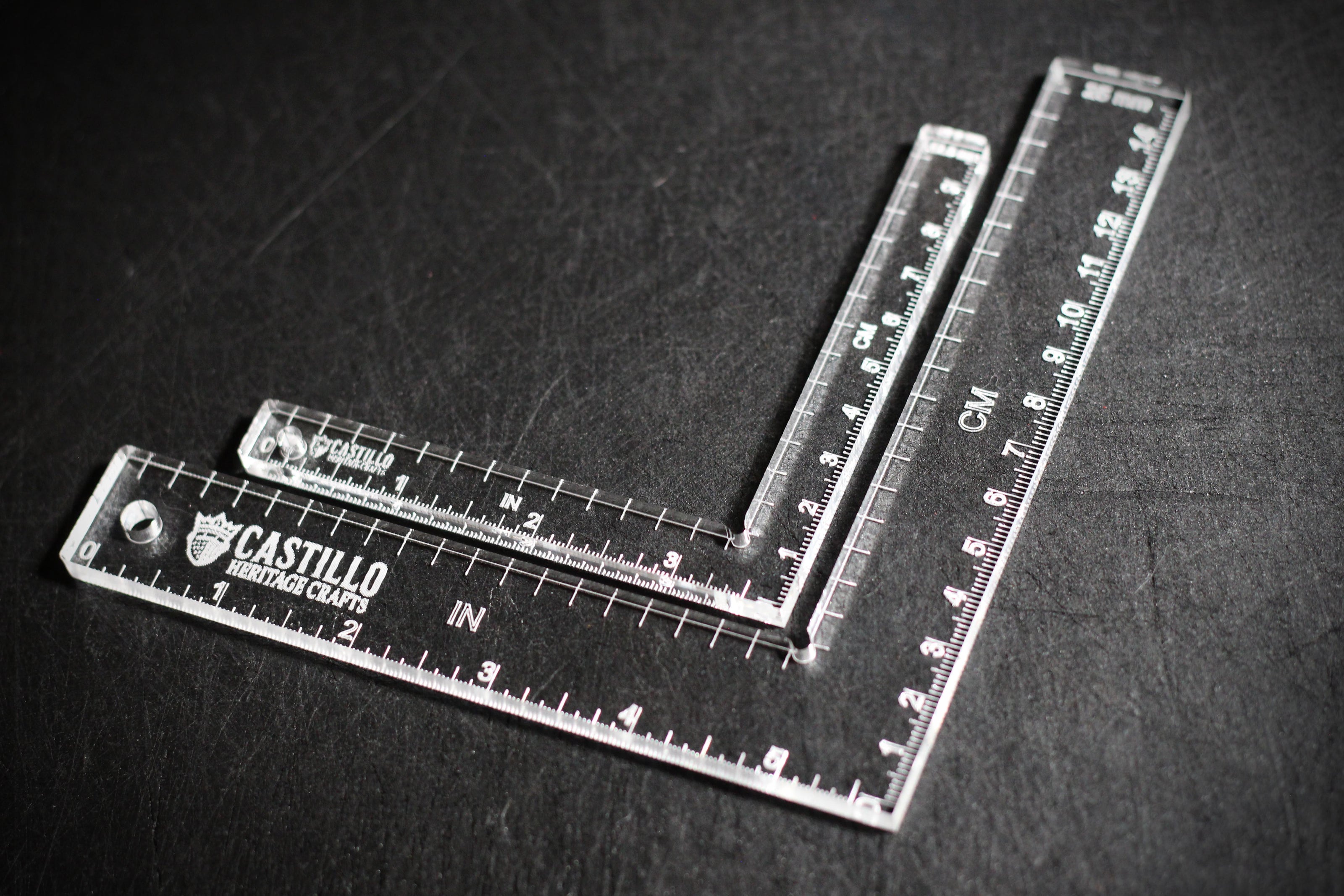 Two clear plastic right angle rulers with measurement markings on a dark surface with 'Castillo Heritage Crafts' branding