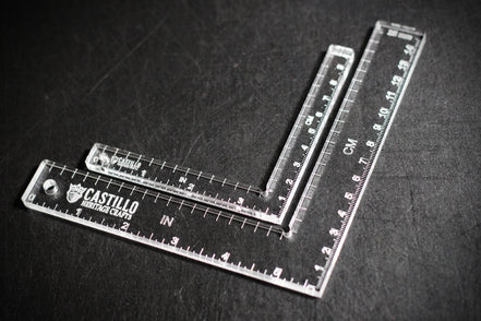 Two clear plastic right angle rulers with measurement markings on a dark surface with 'Castillo Heritage Crafts' branding