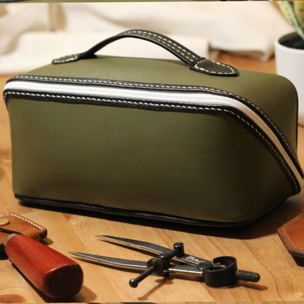 Handmade leather dopp kit made using a DIY pattern surrounded by leathercraft tools on a wooden table