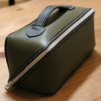 Handmade leather dopp kit made using a DIY pattern surrounded by leathercraft tools on a wooden table