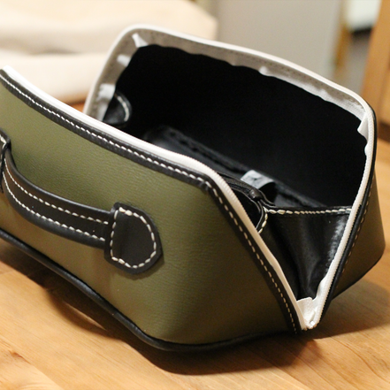 Handmade opened leather dopp kit made using a DIY pattern surrounded by leathercraft tools on a wooden table
