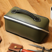 Handmade leather dopp kit made using a DIY pattern surrounded by leathercraft tools on a wooden table
