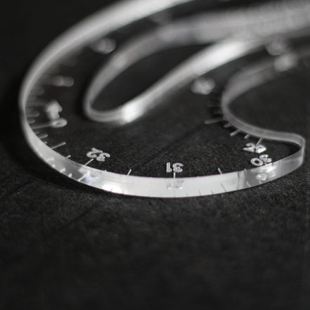A close-up of a clear plastic protractor with angle markings, resting on a dark textured surface.
