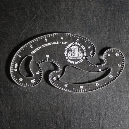 A clear plastic French Curve No. 3 measuring tool by Castello, shown on a dark textured background.