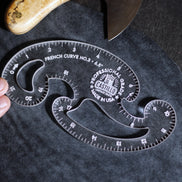 A clear acrylic French curve ruler, model No. 3 by Castillo, shown being held by a hand on a dark textured surface with a knife partially visible in the background.