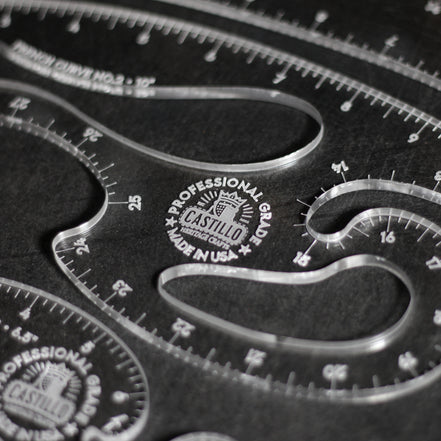 Close-up of a clear acrylic drafting ruler set with curved measurement guides and engraved Castilio branding on a dark background.