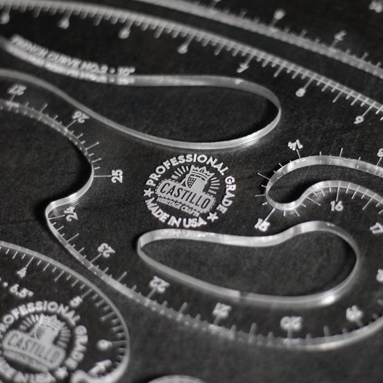 Close-up of a clear acrylic drafting ruler set with curved measurement guides and engraved Castilio branding on a dark background.
