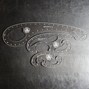 Three clear plastic French Curve Ruler sets of different sizes arranged on a dark, scratched metal surface.