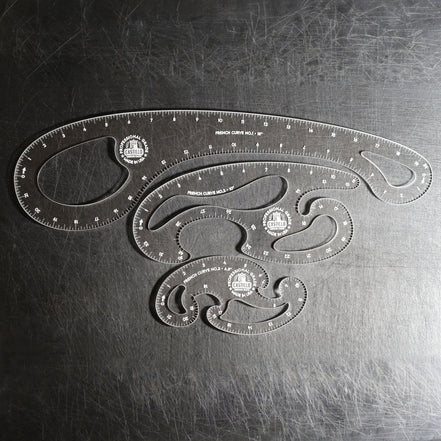 Three clear plastic French Curve Ruler sets of different sizes arranged on a dark, scratched metal surface.